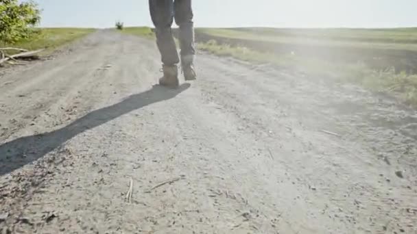 Hombre caminando a lo largo de un camino de tierra a través de tierras agrícolas — Vídeos de Stock