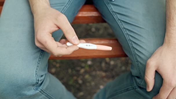 Positieve zwangerschapstest in handen van een jonge jongen in het park. Neutrale reactie. Close-up. Ruwe videoverslag. — Stockvideo
