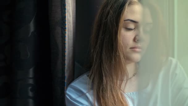 Hermosa chica triste junto a la ventana en un día soleado. De cerca. Grabación de vídeo RAW . — Vídeo de stock