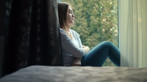 Menina adolescente bonita triste sentado no peitoril da janela. Gravação de vídeo RAW . — Vídeo de Stock