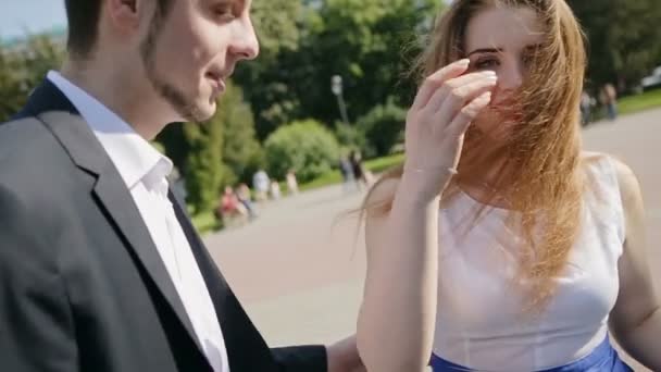 Happy νεαρό ζευγάρι περπάτημα σε ένα πάρκο καλοκαίρι όπου ο άνεμος βολάν τα κορίτσια τα μαλλιά. RAW εγγραφή βίντεο. — Αρχείο Βίντεο