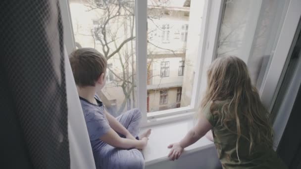 Dvě malé děti dívat skrz okno — Stock video
