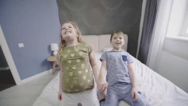 Glada lekfulla flicka och pojke floppa på en säng — Stockvideo