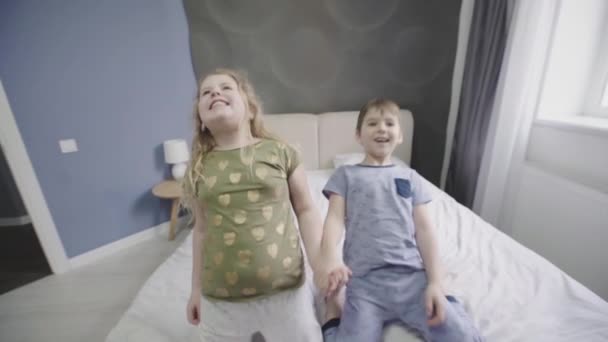 Fröhliche verspielte Mädchen und Jungen, die auf einem Bett floppen — Stockvideo