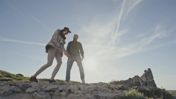 Пара счастливых туристов, прыгающих от радости на вершину горы на фоне восхода солнца и ясного голубого неба — стоковое видео