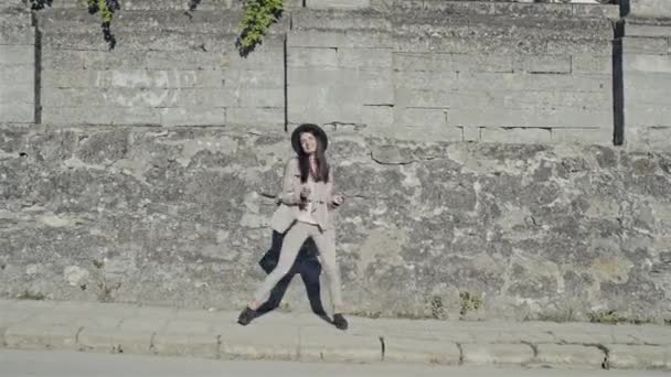 City Lifestyle stilvolles Hipster-Mädchen tanzt lustigen Tanz vor dem Hintergrund einer alten Steinmauer in einer Straße — Stockvideo