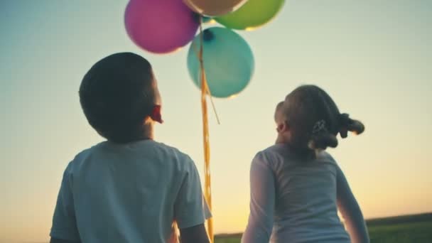 Menino com menina feliz escalar o pôr do sol segurando balões nas mãos. Gravação de vídeo RAW . — Vídeo de Stock