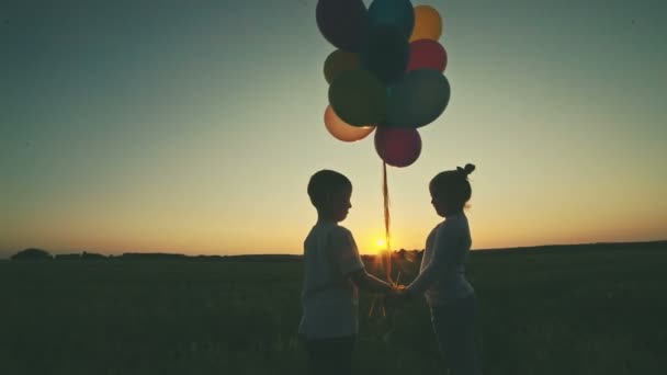 El niño con la niña se abraza sobre un fondo de una puesta de sol sosteniendo globos en las manos. Grabación de vídeo RAW . — Vídeos de Stock