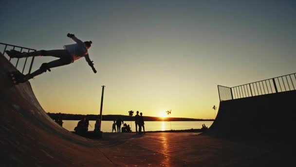 Sylwetka skate rolkach w parku roller, dwóch nastolatków wykonywać złożone skoki na tle zachodzącego słońca. — Wideo stockowe