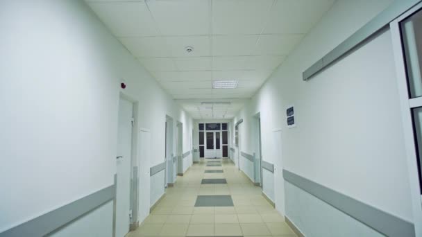 Walking slowly down a corridor hospital hall way with tiled floor and doors leading off on either side with white walls and ceiling — Stock Video