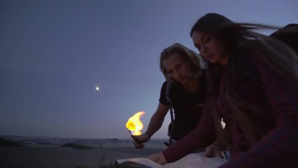 Pareja joven usando una antorcha encendida para leer un mapa al atardecer en el desierto durante un viaje de senderismo con mochilas . — Vídeo de stock