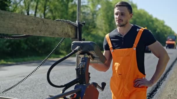 Hombre guapo en uniforme usando el panel de control del vehículo de ingeniería moderno durante las obras de carretera en el día soleado — Vídeos de Stock