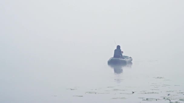 Back view of unrecognizable person sitting on boat and fishing in calm misty morning — Stock Video