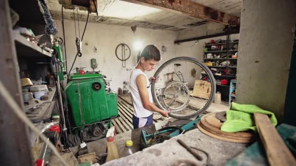 Young poor boy repairs his bike in an old studio. — Stock Video