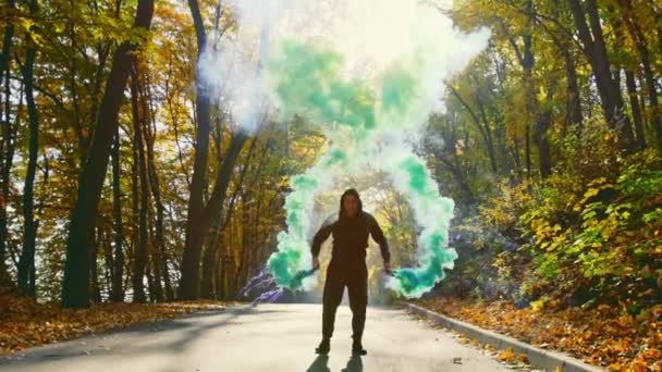 英俊的家伙在运动的手与烟雾耀斑, 然后跑向相机沿沥青路面在晴朗的天在秋季森林. — 图库视频影像
