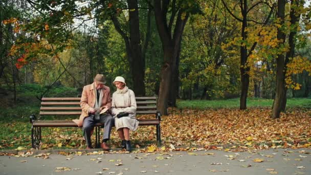 Homem idoso e mulher sentados no banco no incrível parque de outono e lendo carta juntos - movimento dolly . — Vídeo de Stock