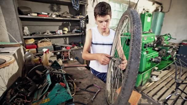 Хлопчик-підліток прикручує велосипедне колесо — стокове відео