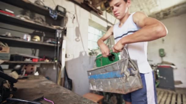 Мальчик-подросток с тяжелым ящиком для инструментов в мастерской — стоковое видео