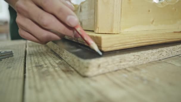 Workman drawing a line around a wooden crate with a pencil onto a piece of chipboard in a close up view of his hands — Stock Video