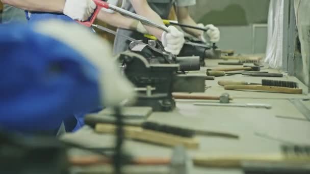 Fila de trabajadores que trabajan con sierras manuales sobre un banco de trabajo lleno de herramientas en una línea de producción de fábrica en un primer plano vista de bajo ángulo — Vídeo de stock