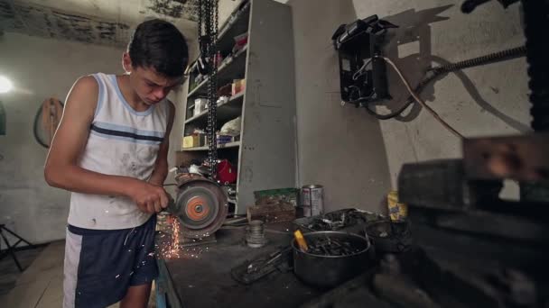 Teenage boy using a grind stone or grinder on metal in a well equipped workshop with a shower of fiery sparks. — Stockvideo