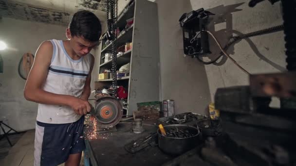 Adolescente usando uma pedra moagem ou moedor de metal em uma oficina bem equipada com uma chuva de faíscas de fogo . — Vídeo de Stock