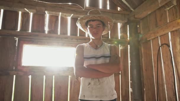 Ragazzo adolescente in cappello di paglia nel fienile contadino, visto da basso angolo, in piedi con e guardando la macchina fotografica, incrociando le braccia e poi uscendo. Ragazzo in cappello di paglia nel fienile — Video Stock