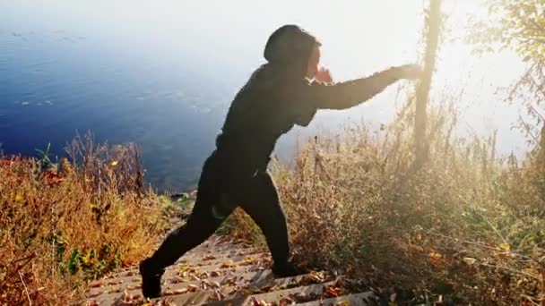 El joven hombre activo entrena en una caja sobre el fondo de un lago en una fría mañana de otoño. Boxeo entrenamiento al aire libre . — Vídeos de Stock