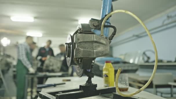 Rotore freno auto in metallo con pinze e tubo sul cavalletto in spaziosa officina . — Video Stock