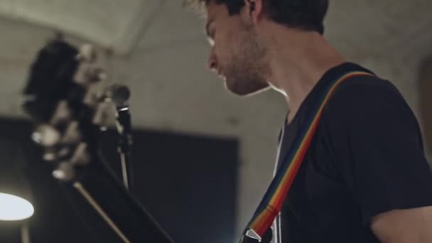 Vista lateral del joven casual tocando la guitarra y cantando mientras está de pie a la luz de las lámparas — Vídeo de stock