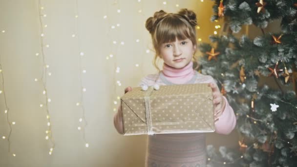 Charmant klein meisje presenteert gewikkeld glimlachend in de camera in gloeiende lichten van de doos van de gift — Stockvideo