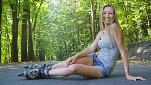 Щаслива красива дівчина з ковзанами сидить на трасі в парку — стокове відео