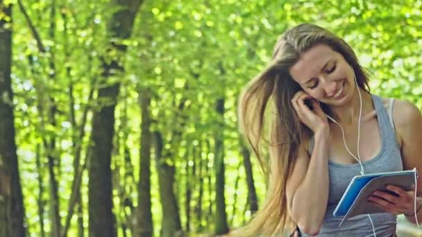 Chica joven escuchando música en el parque y patinaje — Vídeo de stock