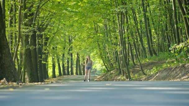 Молодая женщина катается на роликах по летнему лесу — стоковое видео