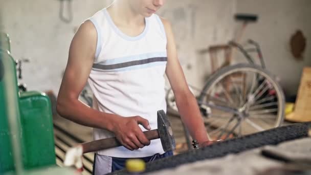 Teenage boy repairing bike with hammer in workshop — Stock Video