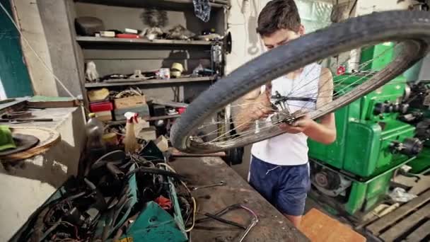 Young teenage boy repairing bike wheel in shed — Stock Video