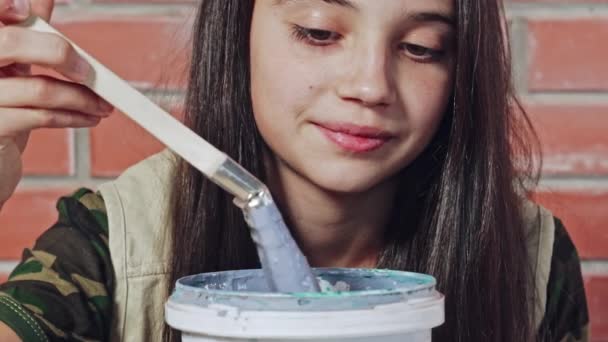 一个好奇的年轻女孩玩画笔和一桶湿油漆的特写 — 图库视频影像