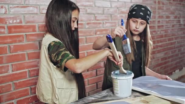 Dos chicas, felices, jóvenes y creativas, vestidas de artistas, pintando en un taller - cámara lenta . — Vídeos de Stock