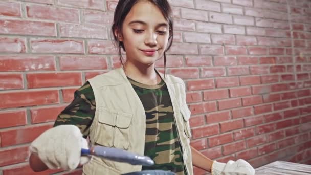 Εφηβικό κορίτσι φορώντας μια ζωγραφική του στέκεται γάντι με γκρι χρώμα από ένα μπάνιο σε ένα ξύλινο τραπέζι κοιτώντας ψηλά να χαμογελά στη φωτογραφική μηχανή - αργή κίνηση. — Αρχείο Βίντεο