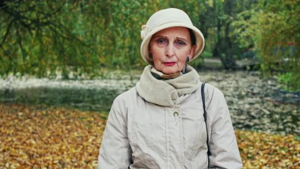 Känslomässiga porträtt av en ensam senior kvinna tittar på kameran med sorg samtidigt lider av depression och ångest utomhus i parken under hösten. — Stockvideo