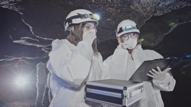 两名身穿生物危害服 戴口罩的女科学家在地下隧道或岩洞内测试和取样毒素 — 图库视频影像