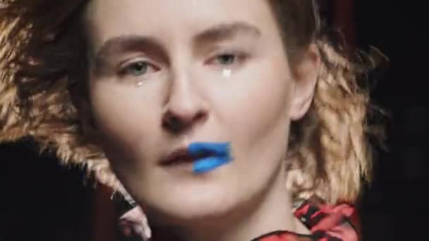 Cara de una joven rubia atractiva de moda con maquillaje moderno y labios medio azules y pelo rizado bailando a un ritmo en un primer plano en su cara — Vídeos de Stock