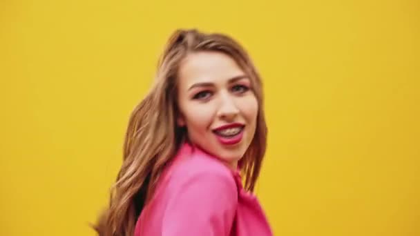 Młoda kobieta z długimi blond włosami różowy top taniec na tle żółty studio machając jej ramiona do muzyki i aparat w zamknąć widok w kierunku na sobie. — Wideo stockowe
