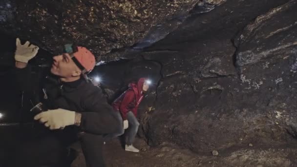 Группа людей с яркими фарами входит в темную пещеру и касается поверхности камня во время спелеологической экспедиции — стоковое видео