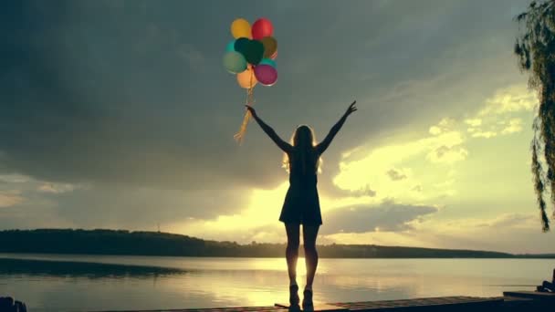 Een jong meisje met ballonnen springen op de achtergrond van de bewolkte hemel bij zonsondergang. Slow motion. — Stockvideo