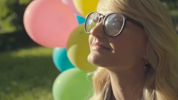 Flicka med ballonger i naturen att göra ansikts uttryck och visar tungan. Råa videoinspelning. — Stockvideo