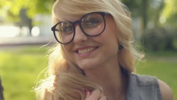 Bright beautiful girl in glasses with beautiful hair smiling at the camera in a summer park at sunset. RAW video record. — Stock Video