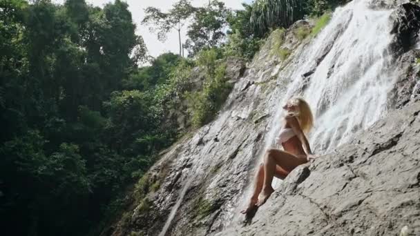 Vrouw in bikini schudden hoofd vergadering tegen waterval — Stockvideo