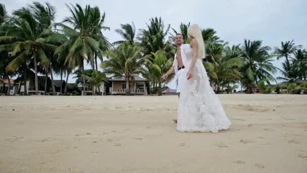 Couple en blanc flânant le long d'une plage de sable fin — Video