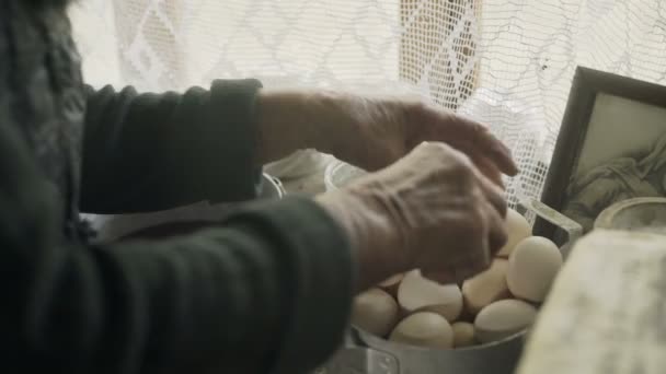 Arme oude grootmoeder neemt eieren bij het raam — Stockvideo